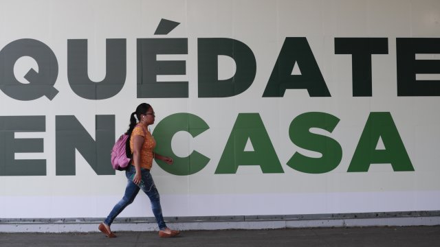 A woman walks past a sign that reads in Spanish "Stay home" in Mexico City, Tuesday, March 31, 2020.
