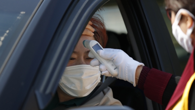 A woman wearing a face mask has her temperature checked upon her arrival for a Sunday drive-in worship service