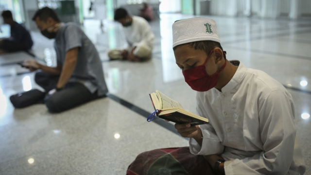Muslim men in Indonesia wearing face masks read the holy book of Quran