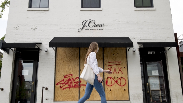 A woman walks past a boarded up J. Crew storefront