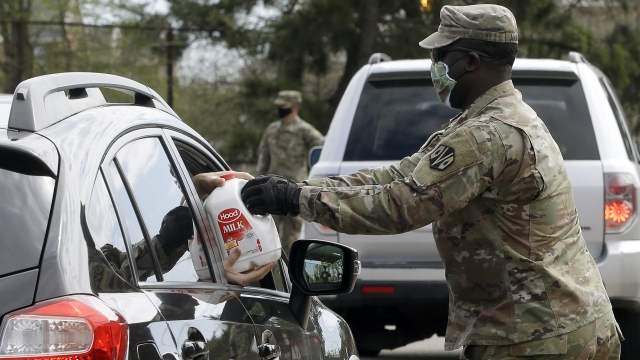 A Massachusetts U.S. Army National Guard soldier hands a gallon container of milk to a recipient in a vehicle