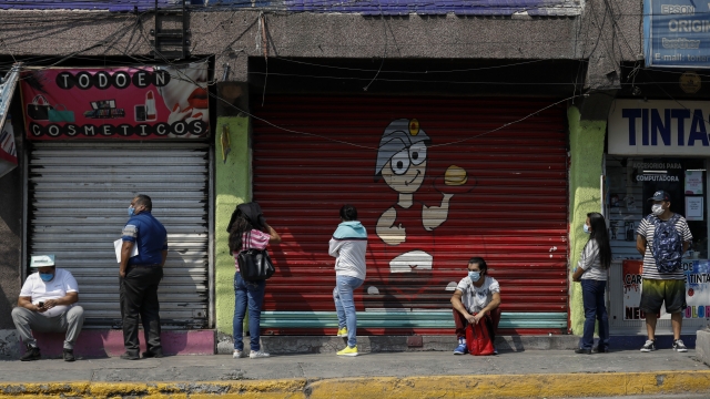 Residents of Mexico City suburb social distance in line to enter bank near shuttered shops.
