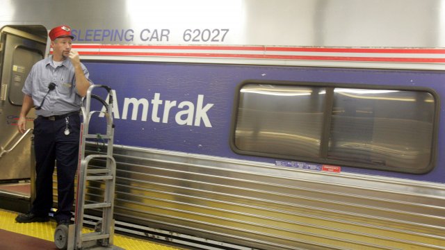 A skycap stands next to an Amtrak train.