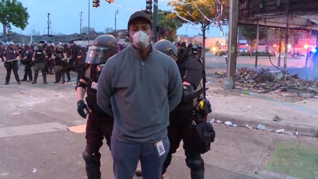 Journalist wearing a mask being handcuffed by police