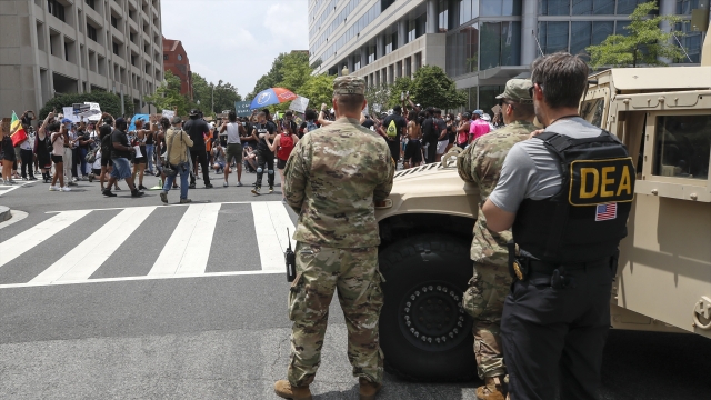 Drug Enforcement Agency police officer and National Guard soldiers watch, demonstrators protest in Washington, D.C.