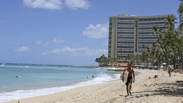 A surfer walks on a sparsely populated Waikiki beach in Honolulu.