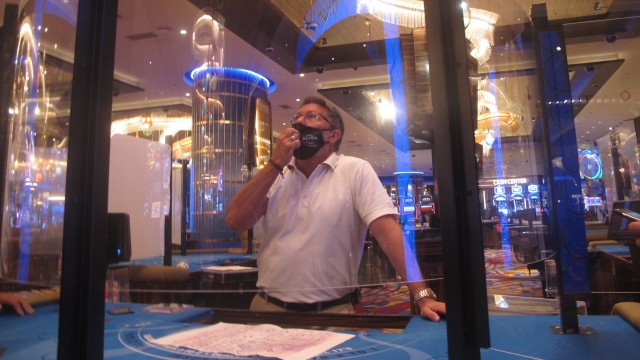 Man examines protective barriers at a casino card table
