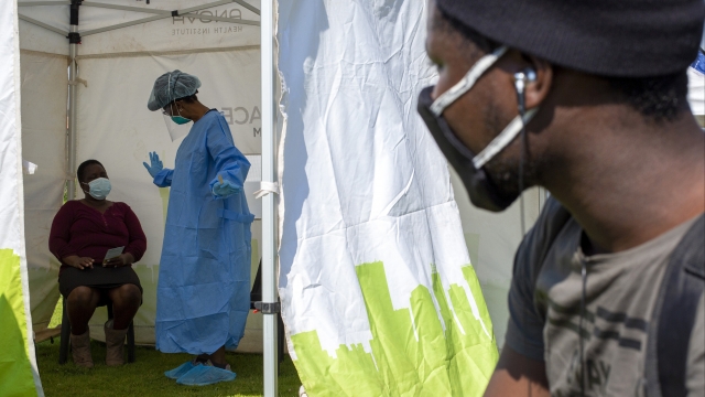A man looks into a tent as a health worker in protective gear collects a sample for COVID-19 testing in South Africa