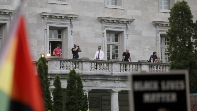 People stand on balcony of mansion of Mark and Patricia McCloskey on July 3 as protests occur below.