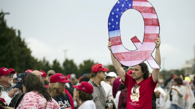 A man holding a Q sign waits in line with others to enter a campaign rally with President Donald Trump.