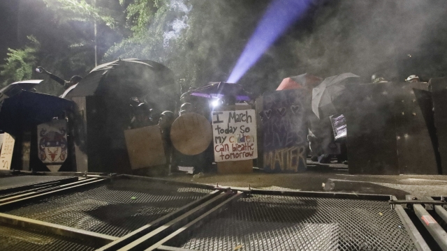 Demonstrators sheild themselves after toppling a fence in Portland, Oregon