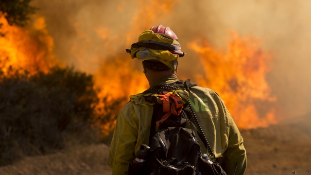 A firefighter watches as flames flare at the Apple Fire in Cherry Valley, Calif.