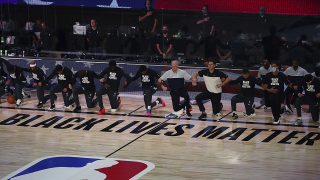 NBA players and coaches lock arms and kneel before an NBA basketball game.