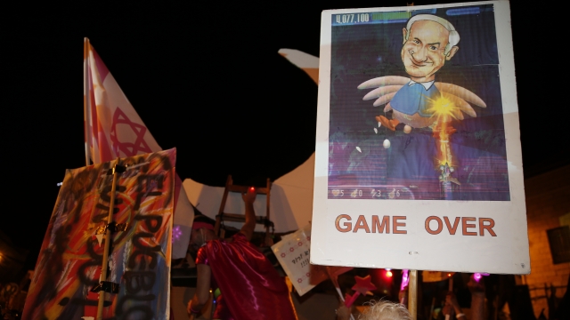 Protester holds sign with PM Netanyahu's face on it. Below the pictures it says "Game Over"