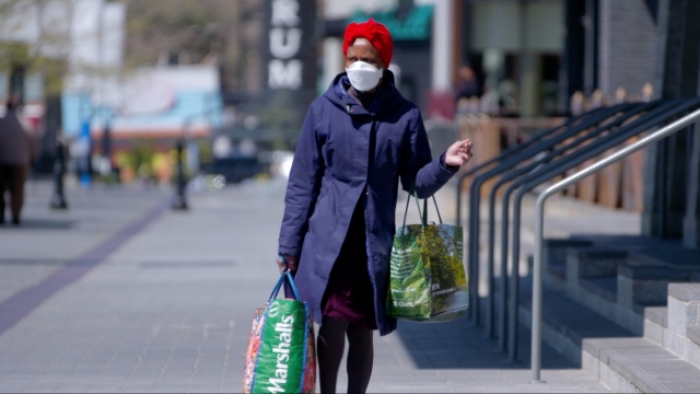 Woman wears a mask and carries shopping bags.