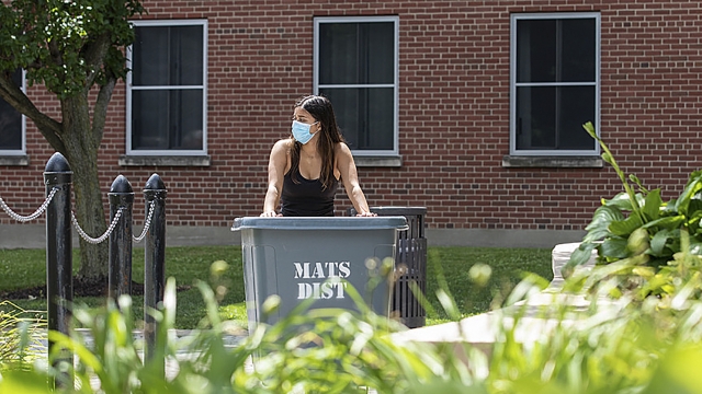 A student wearing a mask wheels her belongings up a ramp to move into her dorm.
