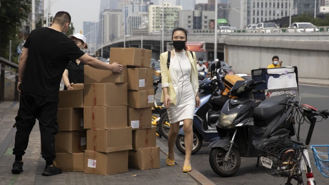 Woman passes delivery workers moving shipping boxes in Beijing.