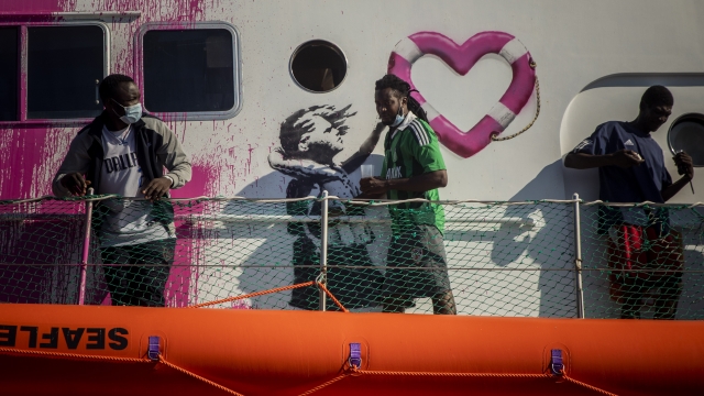 A man walks past a painting by British artist Banksy on the deck of the Louise Michele rescue vessel