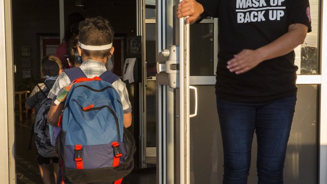 A staff member holds the door open for kids on the first day of school in Texas.
