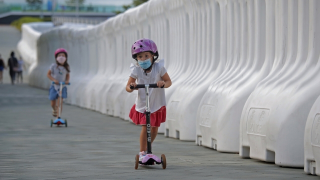 Young children ride scooters down a sidewalk in Hong Kong