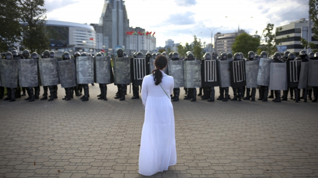 A woman wearing white, stands in front of a riot police line during a Belarusian opposition supporters' rally