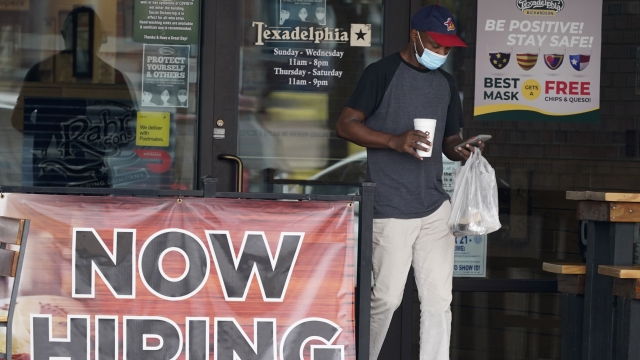 A customer wears a mask and looks at their cell phone as they carry their order past a now hiring sign.