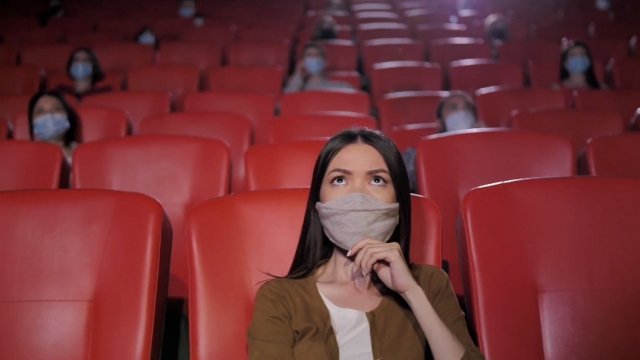 Woman wearing face mask watches a movie at a cinema.
