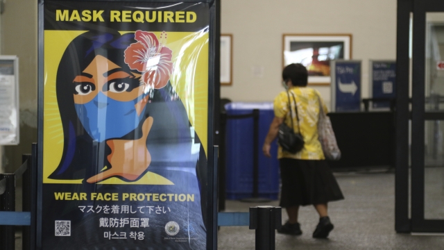 Traveler enters Daniel K. Inouye International Airport in Honolulu, passing sign for mask-wearing requirement on islands.