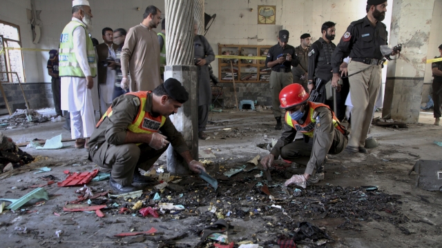 Rescue workers and police officers examine the site of bomb explosion in an Islamic seminary in Peshawar, Pakistan