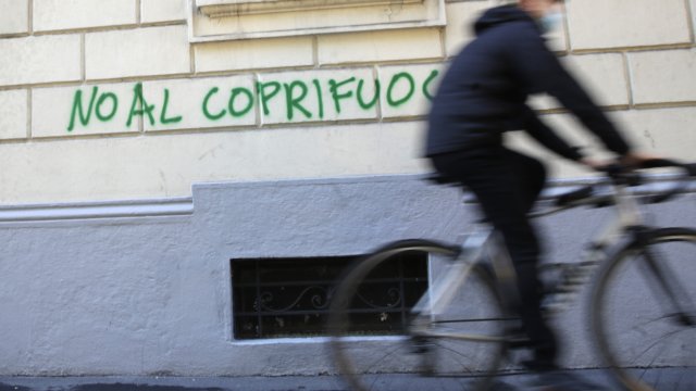 A biker passes by a writing reading "No to curfew", in Milan, Italy