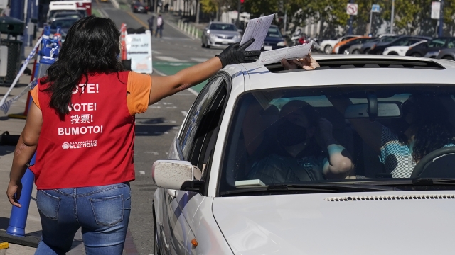 San Francisco Department of Elections voting clerk takes ballots from voters in a vehicle at a drive-up area.