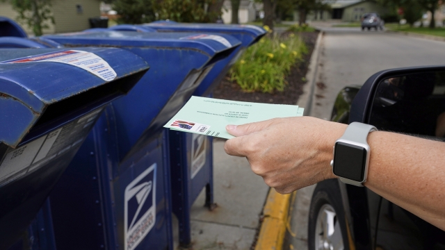 A person drops applications for mail-in-ballots into a mailbox.