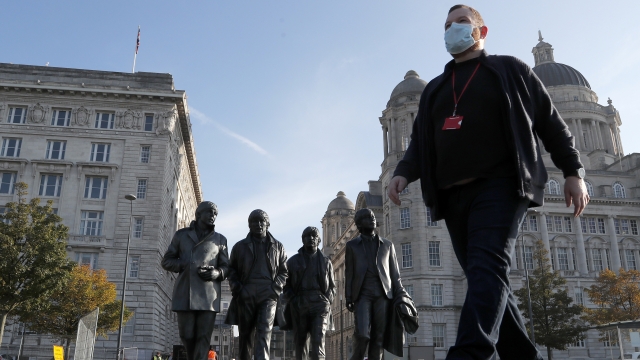 A man wearing a face mask walks past a statue of the Beatles, ahead of new measures in Liverpool, England