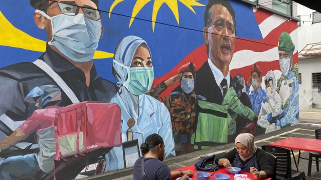 A Malay couple have lunch next to a graffiti tribute to Malaysian workers on the frontlines against COVID-19