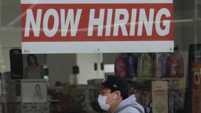 Man wearing a mask while walking under a 'Now Hiring' sign.