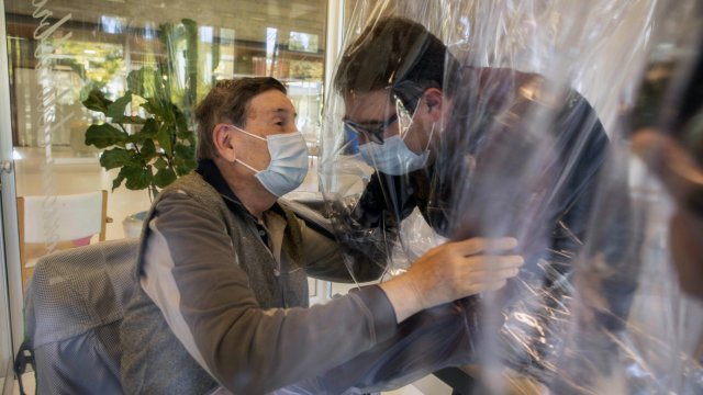 Relatives hug each other through a plastic film screen and a glass to avoid contracting COVID-19, at a nursing home in Italy.