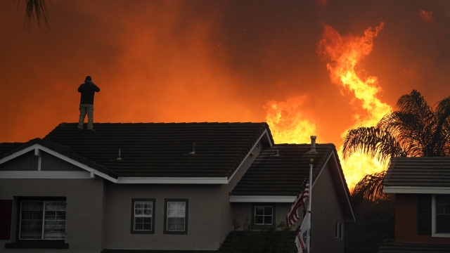A man stands on the roof of his home as the Blue Ridge Fire burns along the hillside in Chino Hills, California