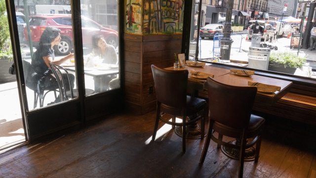 Customers have lunch outside as a table inside sits empty at a restaurant in New York  City