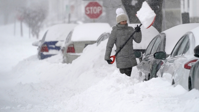 A woman tosses a shovel full of snow while digging out her car