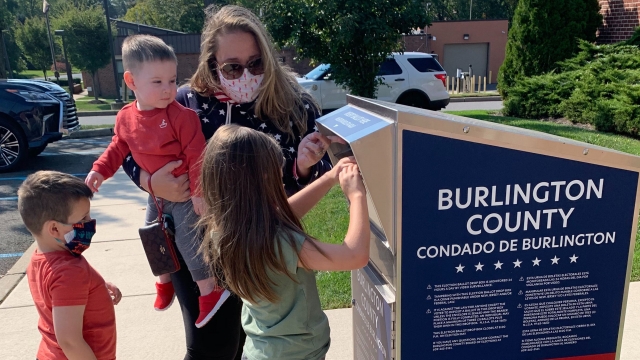 Woman with kids drops ballot in drop box.
