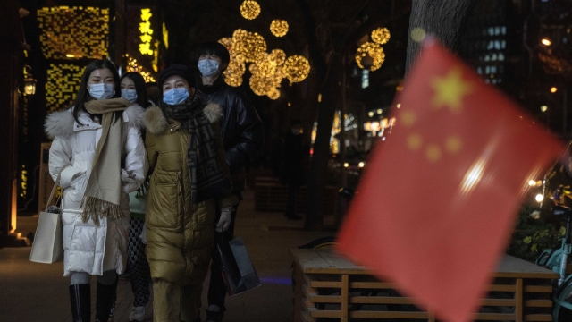 People wearing masks pass by a Chinese national flag