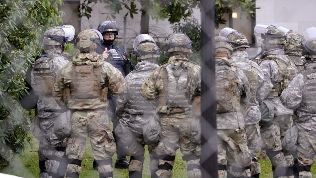 A Washington State Patrol trooper talks with members of the Washington National Guard inside a fence surrounding the Capitol.