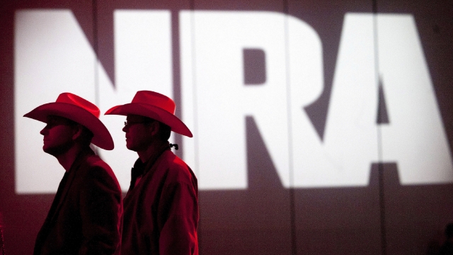 Two cowboy hat wearing NRA members walk in front of the gun groups logo