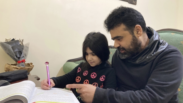 A Syrian refugee helps his daughter with her homework