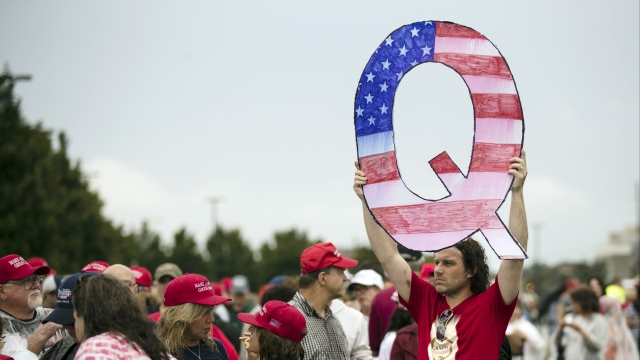 A man holds a giant Q sign at a Trump rally