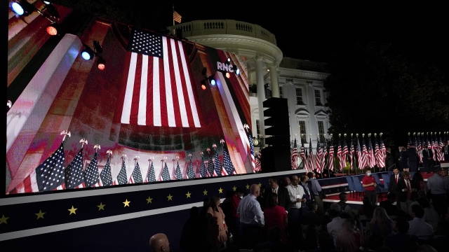 The Republican National Convention video is displayed on a screen as people watch from the South Lawn of the White House.
