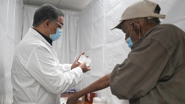 A doctor examines a vaccination card before giving a second dose of the COVID-19 vaccine