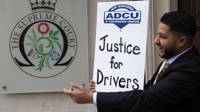 Uber driver and president of the (ADCU), App Drivers & Couriers Union, Yaseen Islam poses with a poster outside the Supreme C