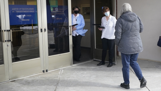 A LabCorp worker, second from right, greets a person, right, at an entrance to a COVID-19 vaccination site.