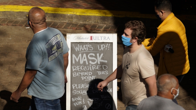 Visitors wearing face masks walk past a sign requiring masks